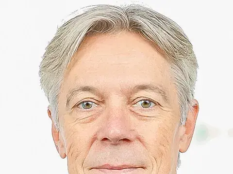 Ein grauhaariger Mann mittleren Alters im dunklen Sakko blickt lächelnd in die Kamera.