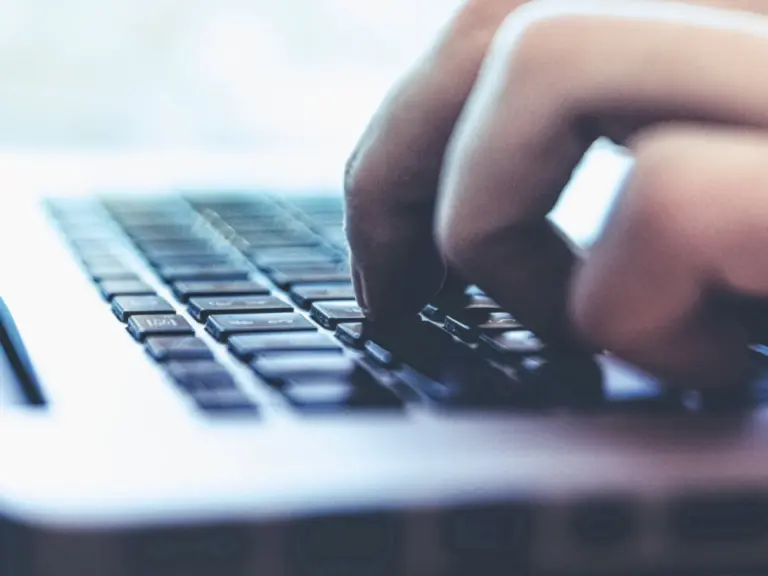 Eine Hand tippt auf der Tastatur eines Laptops, Nahaufnahme mit unscharfem Hintergrund.