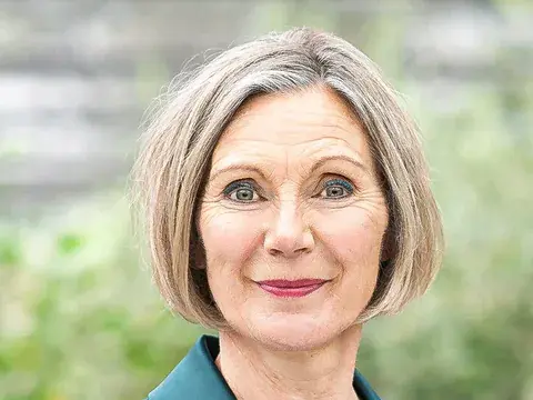 Eine Frau mittleren Alters mit schulterlangem, grauem Haar in dunkelgrünem Blazer blickt lächelnd in die Kamera.