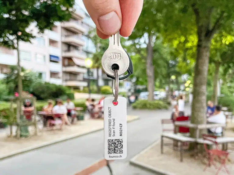 Eine Hand hält einen Schlüssel mit einem Anhänger mit QR-Code in die Luft, im Hintergrund ein Park.