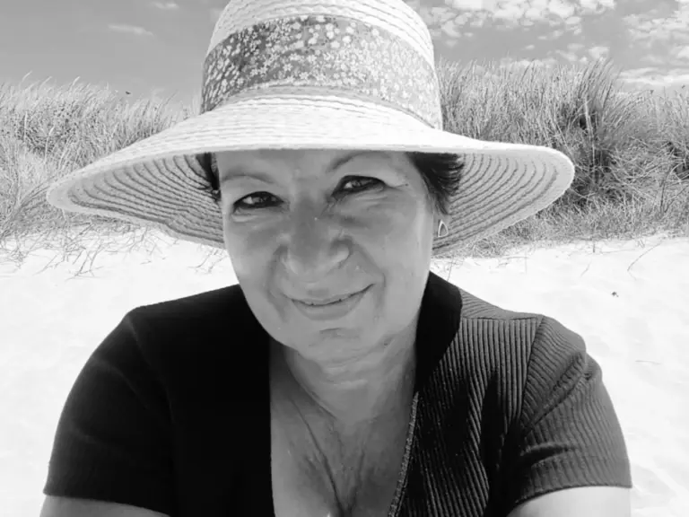 Lächelnde Frau mit Sonnenhut sitzt an einem Sanddünenstrand, Schwarzweissfoto.