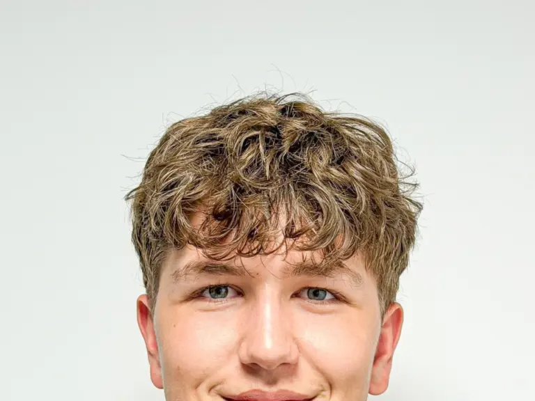 Junger Mann mit lockigem Haar und gestreiftem Poloshirt lächelt leicht in die Kamera.