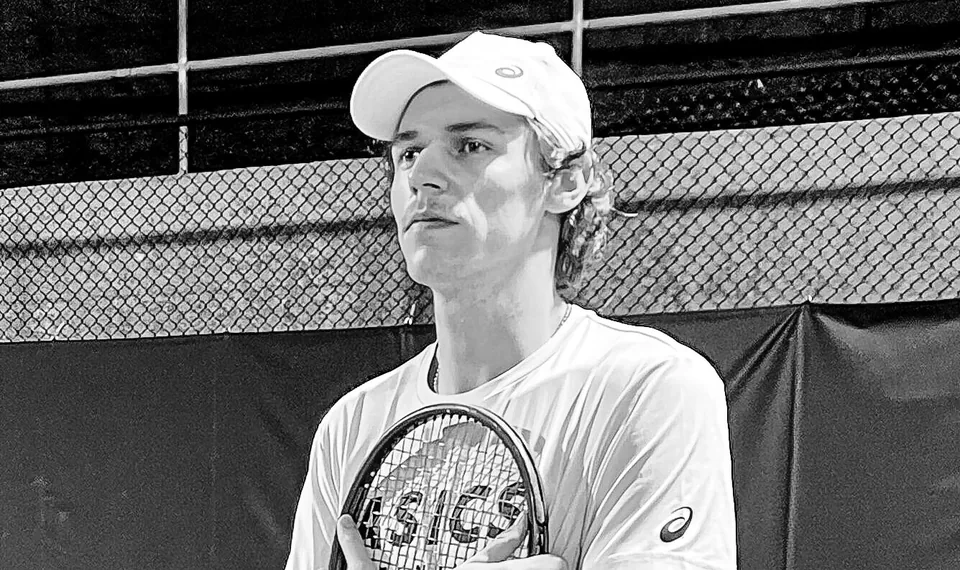 Ein junger Tennisspieler mit Cap hält einen Schläger an die Brust und blickt zur Seite, Schwarzweißfoto.