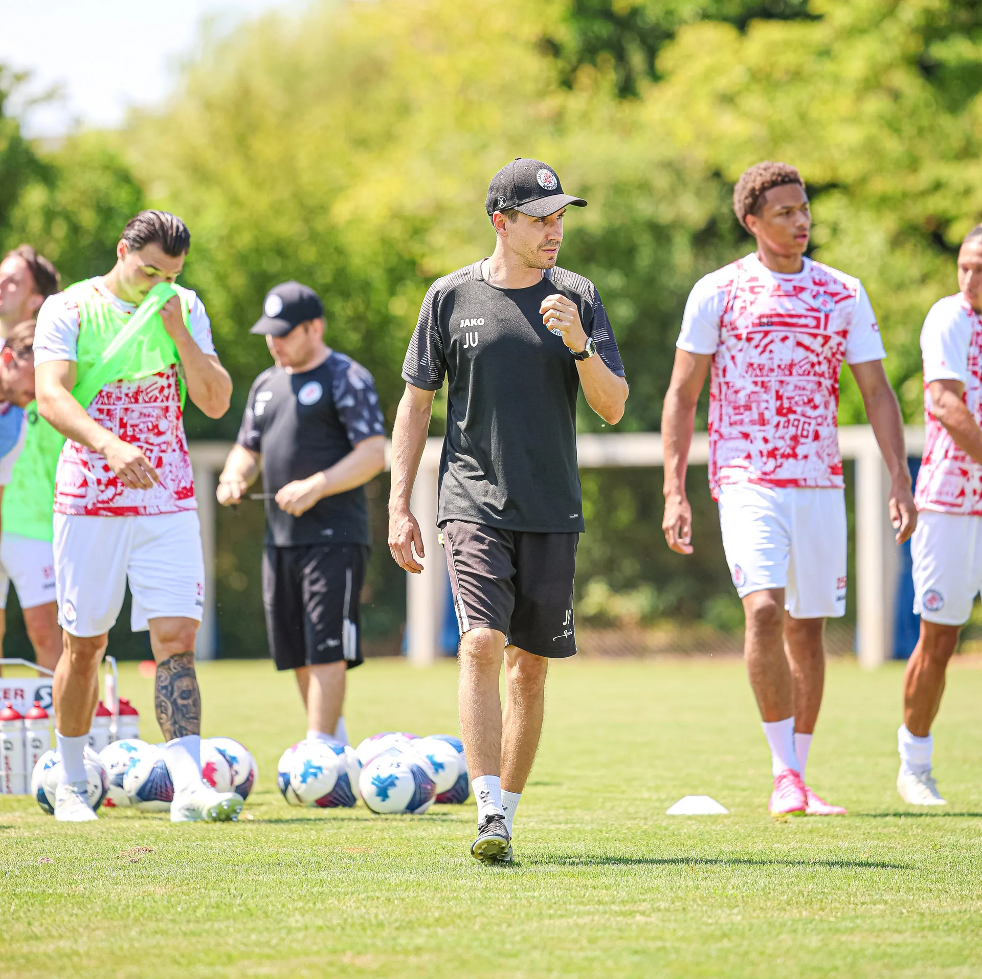 Fussballspieler und ein Trainer laufen bei einem Training über einen Rasenplatz.