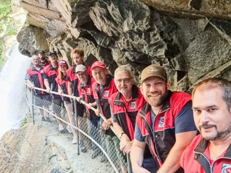 Eine Gruppe von Menschen in roten Westen steht entlang eines schmalen Felsenpfads neben einem Wasserfall.