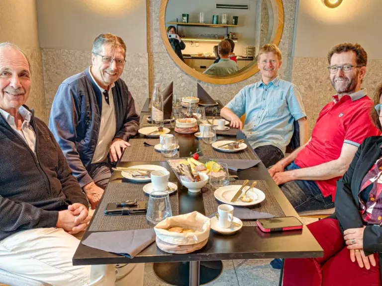 Fünf Erwachsene sitzen lächelnd an einem gedeckten Tisch in einem Café.