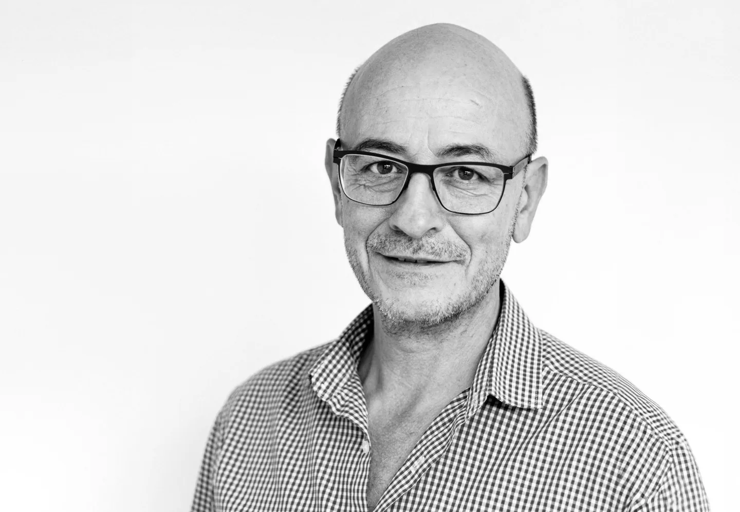 Ein älterer Mann mit Brille, Halbglatze und kariertem Hemd blickt lächelnd in die Kamera.