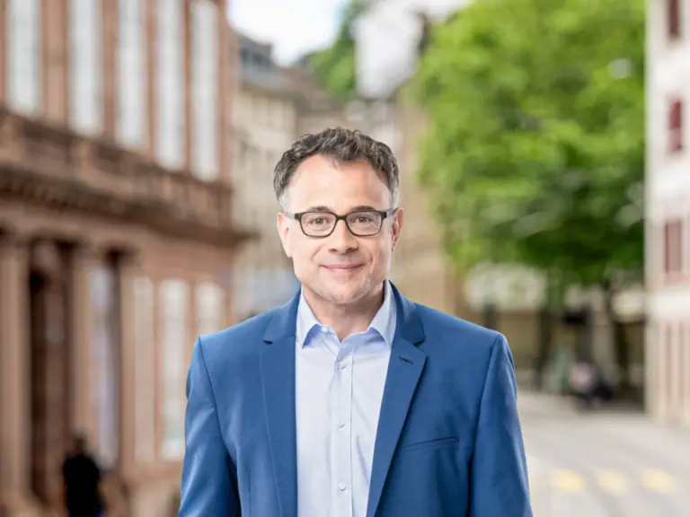 Ein lächelnder Mann mit Brille und blauem Sakko steht auf einer Straße in der Altstadt.