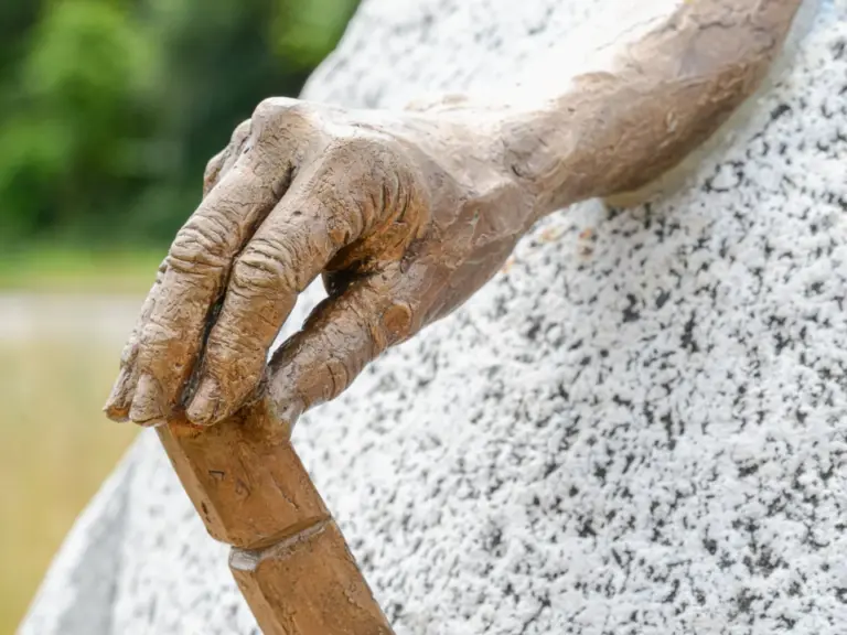 Eine bronzene Hand mit einem Meissel ragt aus einem grossen, runden Steinblock.