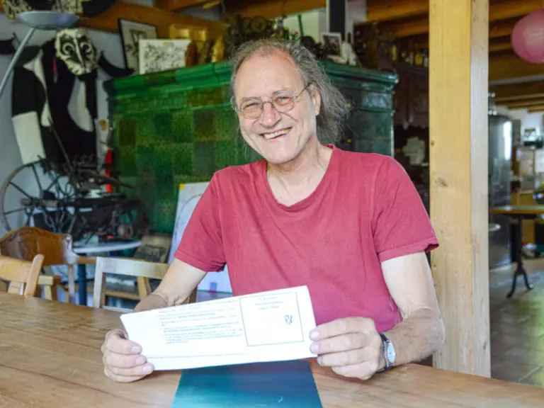 Ein lächelnder Mann mit Brille sitzt an einem Holztisch und hält ein Formular in den Händen.