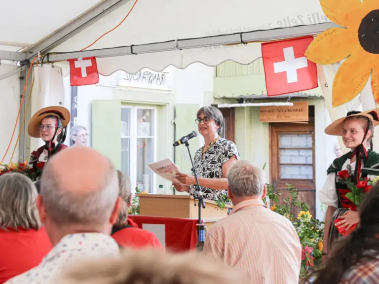 Eine Frau hält am Rednerpult eine Rede, daneben zwei Frauen in Trachten, davor sitzt das Publikum in einem Festzelt.