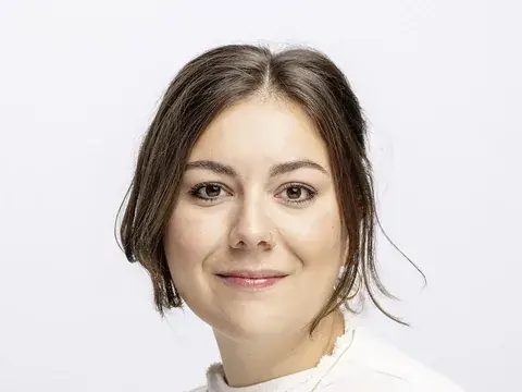 Porträt einer jungen Frau mit dunklen, offenen Haaren, die lächelnd in die Kamera blickt.