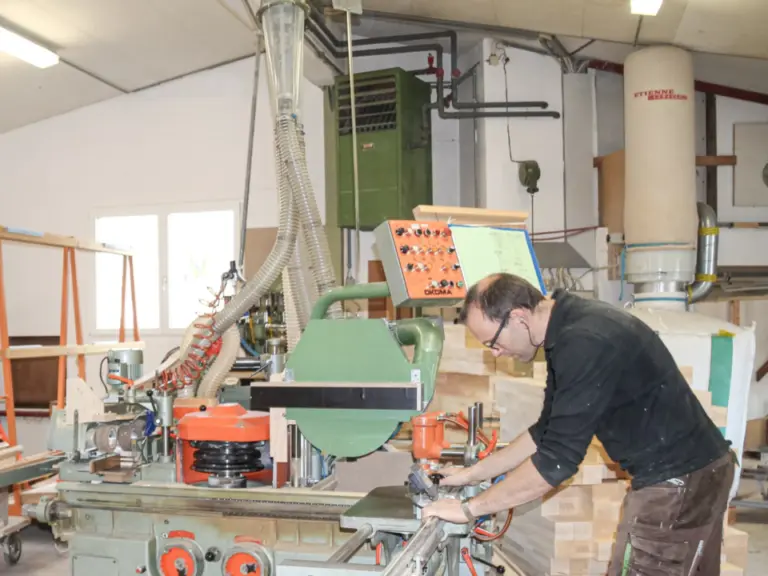 Ein Mann mit Brille bedient eine grosse Holzbearbeitungsmaschine in einer Werkstatt.