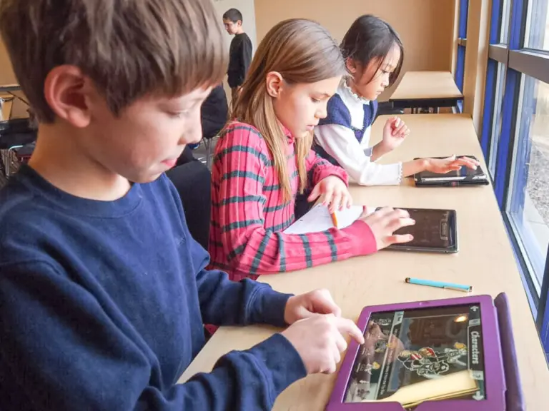 Drei Kinder sitzen nebeneinander an einem Tisch und bedienen Tablets mit den Fingern.