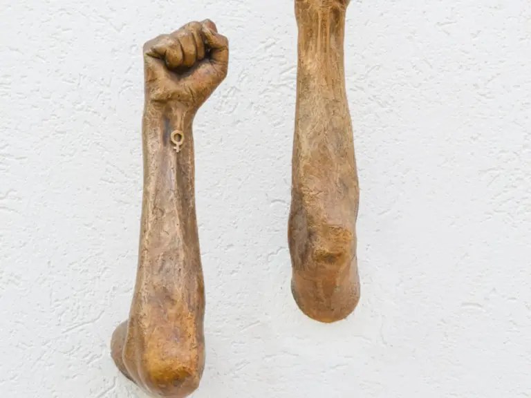Zwei bronzene, erhobene Fäuste ragen aus einer weissen Wand hervor.