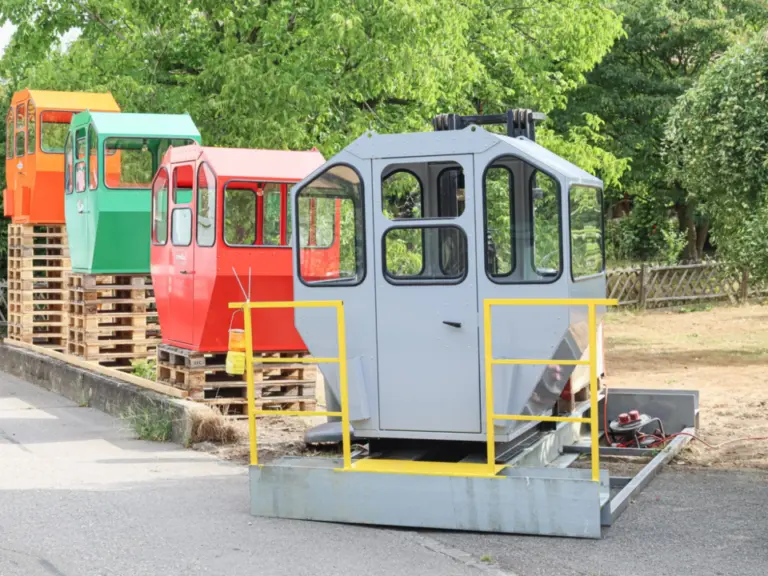 Mehrere bunte Seilbahn- oder Standseilbahnkabinen ohne Fahrgestell stehen aufgereiht am Strassenrand.