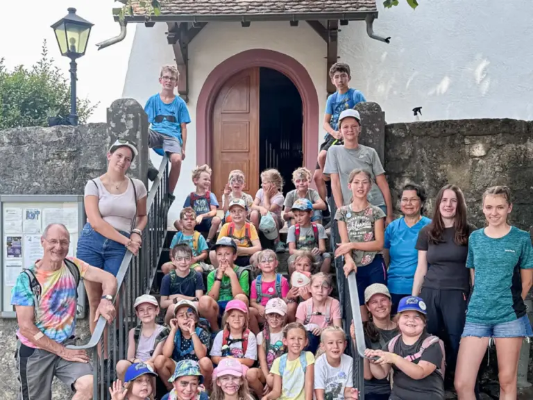 Grosse Gruppe von Kindern und Erwachsenen sitzt und steht auf einer Treppe vor einem Kirchenportal.