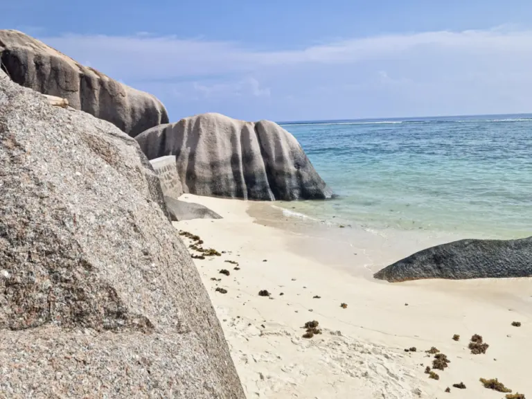Grosse, glatt geformte Granitfelsen ragen an einem weissen Sandstrand neben türkisfarbenem Meer empor.