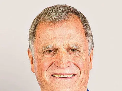 Ein älterer Mann mit grauen Haaren lächelt in die Kamera, er trägt ein blaues Jackett mit weissem Hemd.