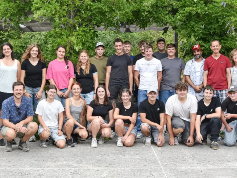 Gruppenfoto mit rund 25 jungen Menschen, stehend und kniend, vor grünen Bäumen auf einem Innenhof.