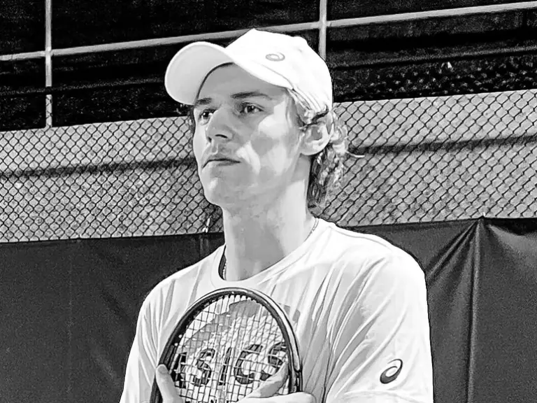Ein junger Mann mit Kappe hält einen Tennisschläger an die Brust und blickt zur Seite.