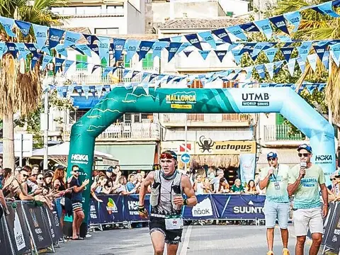 Ein erschöpfter Läufer erreicht das Ziel eines Trailrennens, im Hintergrund applaudieren Zuschauer.
