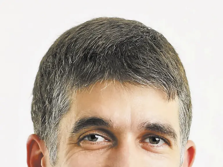 Ein lächelnder Mann mit kurzen grauen Haaren im Anzug und hellblauem Hemd.