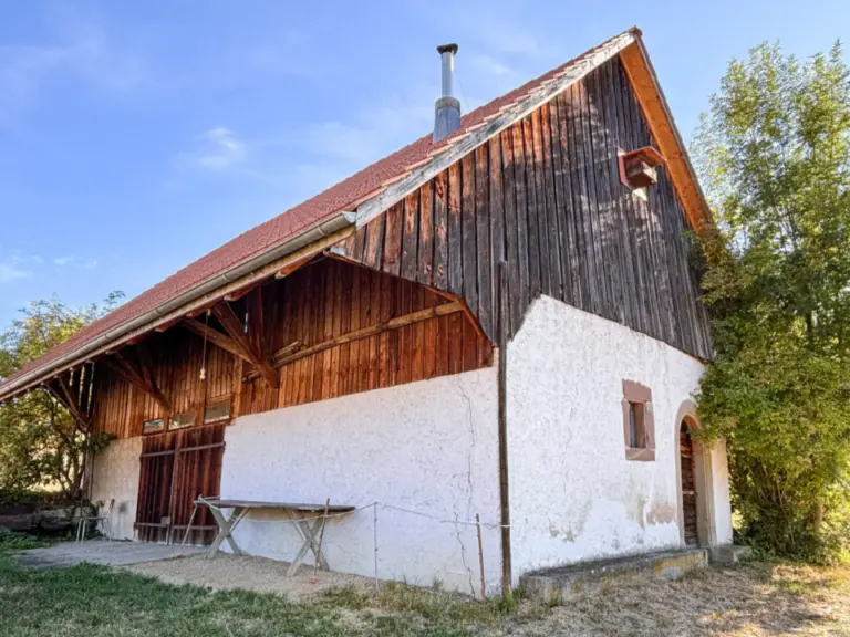 Eine alte Scheune mit Holzfassade und weiss verputztem Sockel unter blauem Himmel.