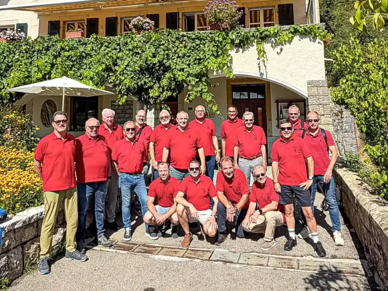 Gruppe Männer in roten Poloshirts posiert vor einem Riegelhaus mit Rebstöcken an der Fassade.