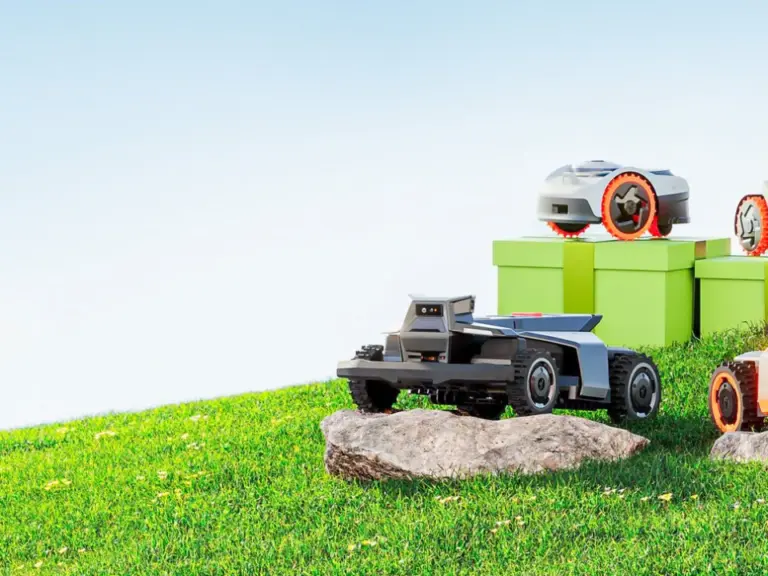 Zwei Mähroboter und weitere kleine Geräte stehen auf einer grünen Wiese neben Steinen.