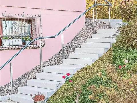 Eine Steintreppe mit geschwungenem Metallgeländer führt an einem rosafarbenen Haus vorbei einen Hang hinauf.