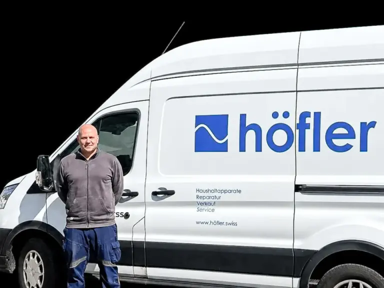 Ein Mann steht lächelnd vor einem weissen Lieferwagen mit dem Logo und Schriftzug „höfler“.