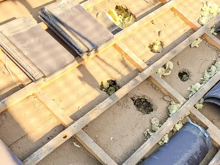 Blick auf ein Dach ohne Ziegel mit sichtbaren Holzlatten, Dämmmaterial und einzelnen losen Dachziegeln.
