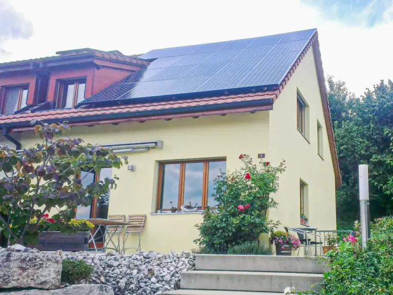 Gelbes Einfamilienhaus mit Solaranlage auf dem Dach und blühendem Garten davor.