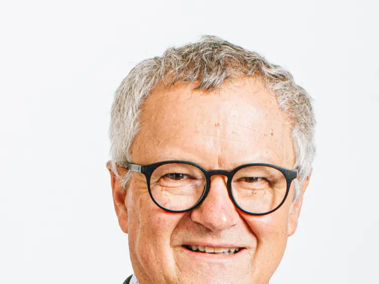 Ein älterer Mann mit grauen Haaren, Brille und Anzug lächelt in die Kamera.