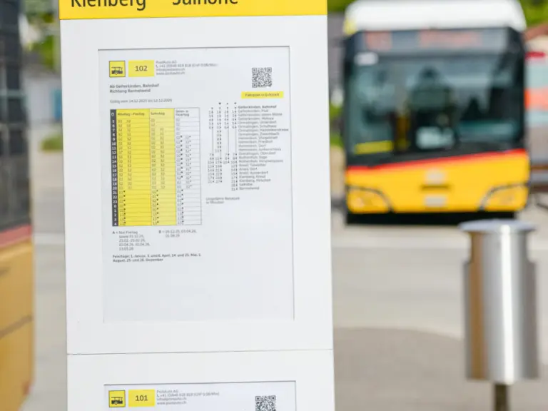 Haltestellenschild mit Fahrplänen der Linien 101 und 102, im Hintergrund ein gelber Bus.