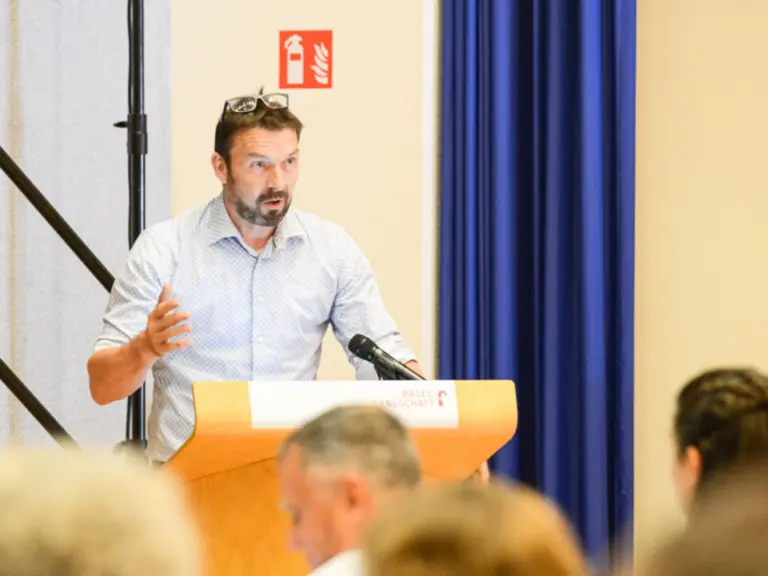 Ein Mann spricht gestikulierend an einem Rednerpult vor sitzendem Publikum in einem Saal.