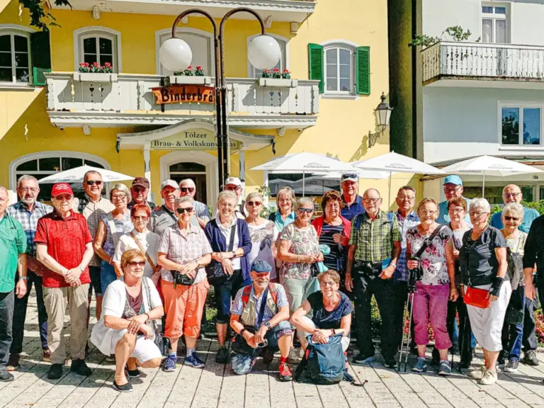 Eine große Gruppe von Menschen steht und kniet für ein Gruppenfoto vor gelben und weißen Gebäuden.
