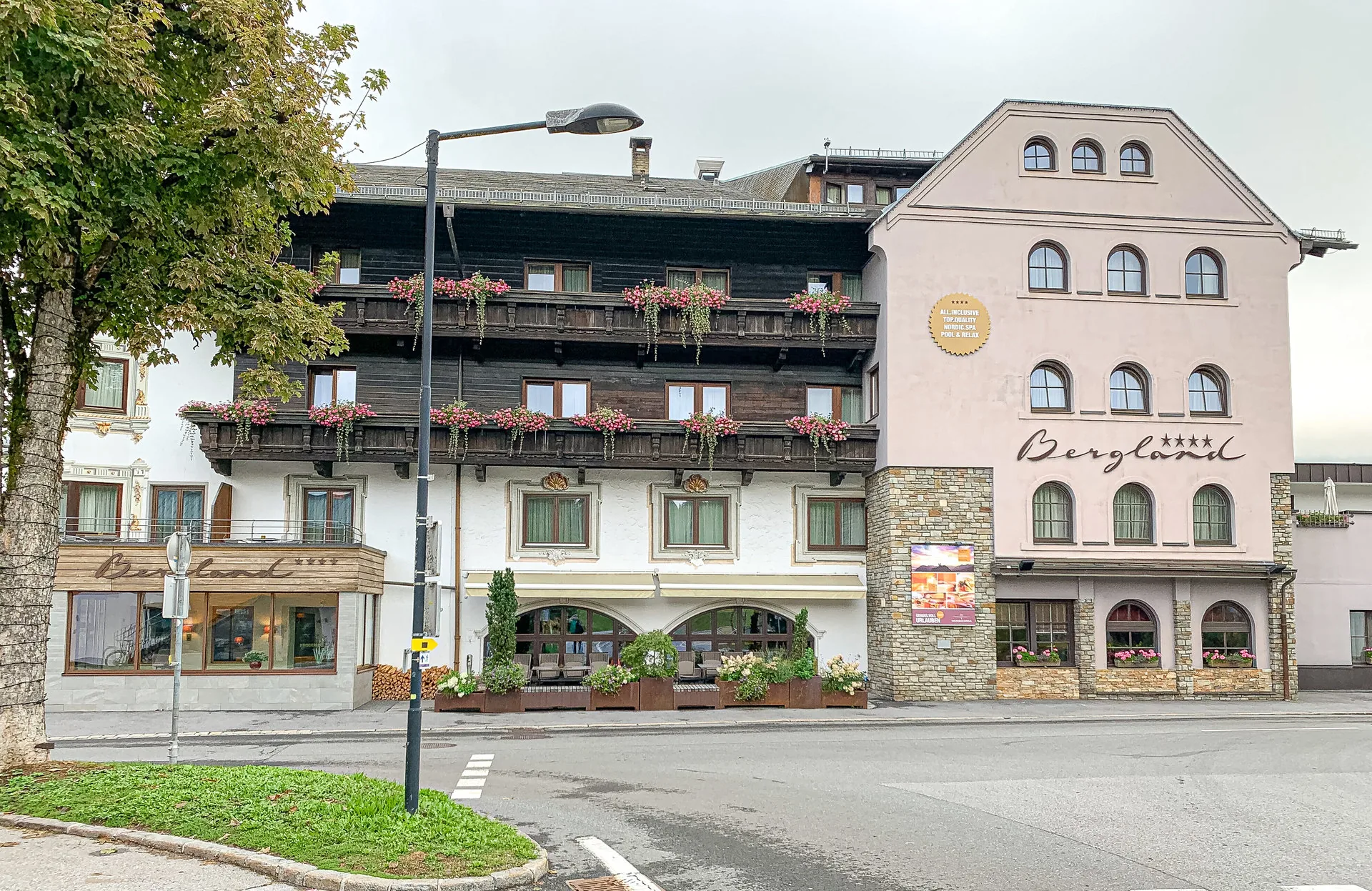 Alpines Hotelgebäude mit Holzbalkonen voller Blumen an einer Straßenkreuzung.