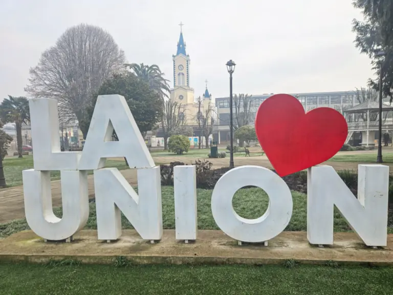 Grosse weisse Buchstaben „LA UNION“ mit rotem Herz auf einer Grünfläche, im Hintergrund eine Kirche.