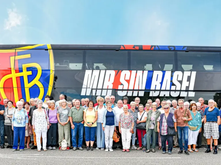 Grosse Gruppe älterer Menschen steht vor einem Doppelstock-Reisebus mit FCB-Logo und Schriftzug «Mir sin Basel».