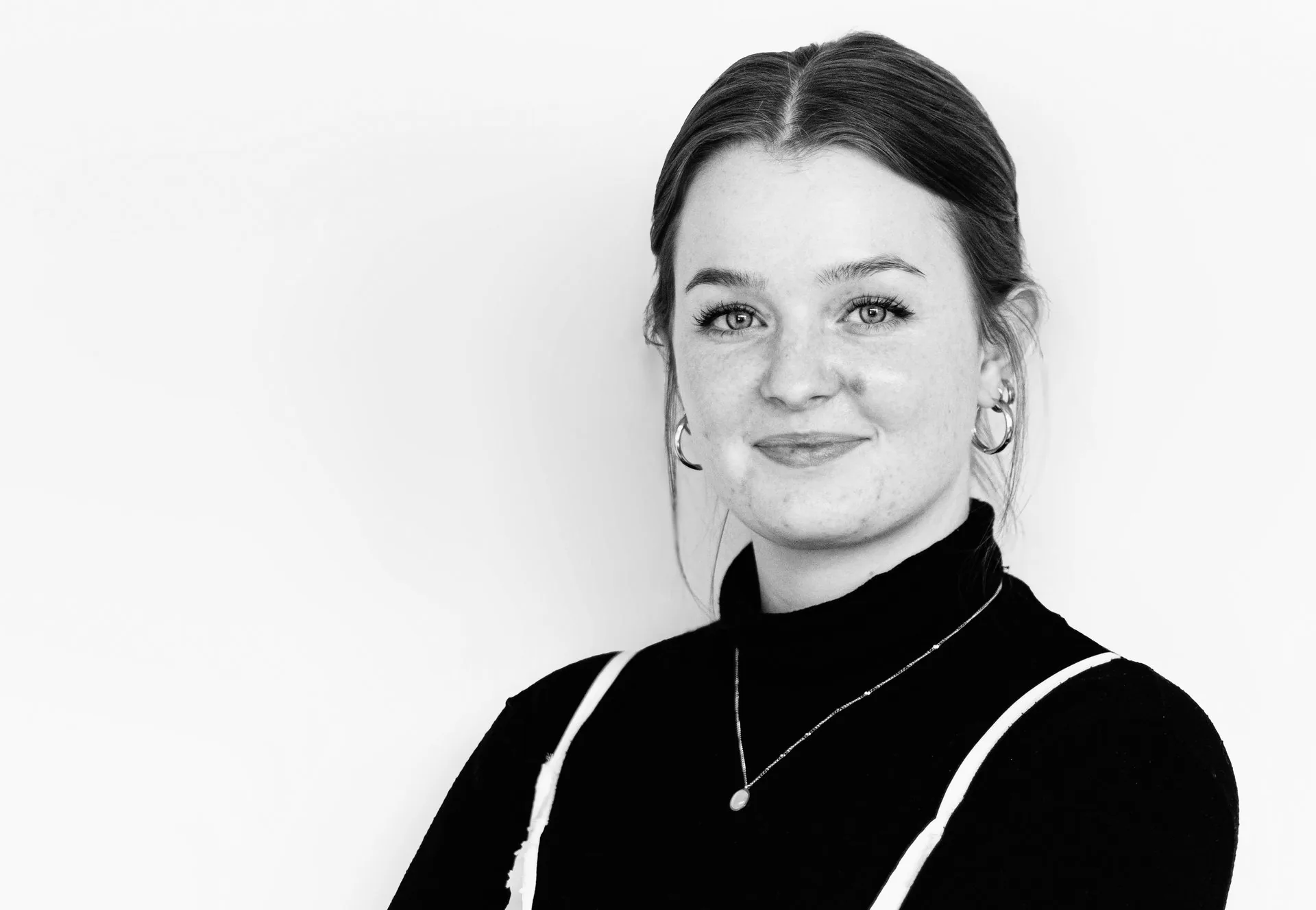 Junge Frau mit zurückgebundenem Haar lächelt leicht in die Kamera, Schwarz-Weiß-Porträt.