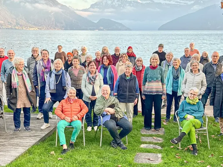 Grosse Gruppe von Menschen posiert für ein Gruppenfoto vor einem See und Bergpanorama.