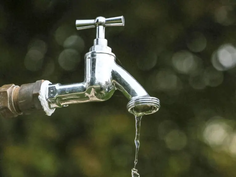 Ein glänzender Wasserhahn mit tropfendem Wasser vor unscharfem grünem Hintergrund.