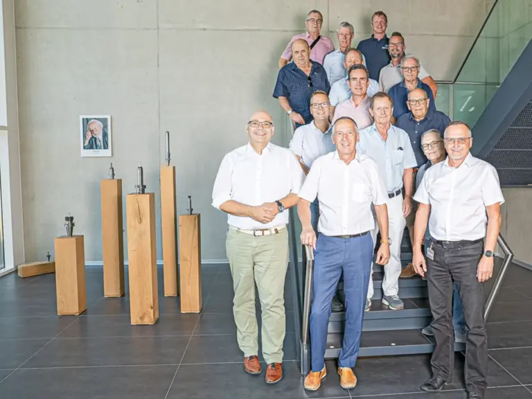 Eine Gruppe von Männern in Freizeitkleidung steht und posiert auf einer Treppe in einer Halle.