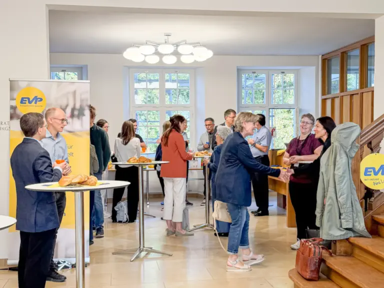 Mehrere Menschen stehen und unterhalten sich in einer hellen Empfangshalle mit Stehtischen und EVP-Bannern.