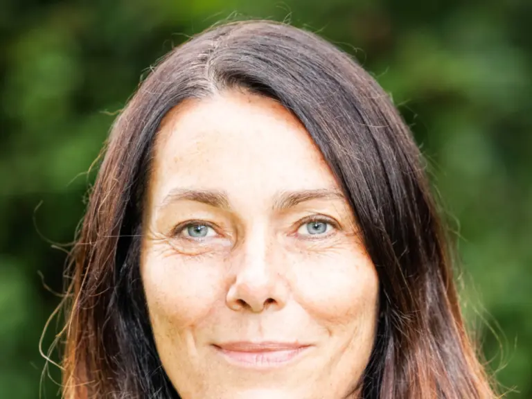 Eine Frau mittleren Alters mit schulterlangen braunen Haaren lächelt leicht vor grünem Hintergrund.