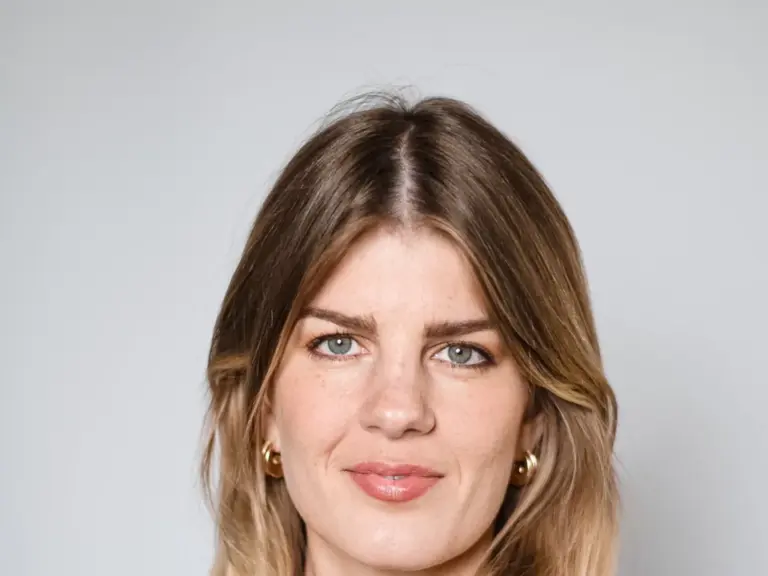 Eine Frau mit schulterlangen blonden Haaren blickt in die Kamera, sie trägt ein dunkles Sakko.