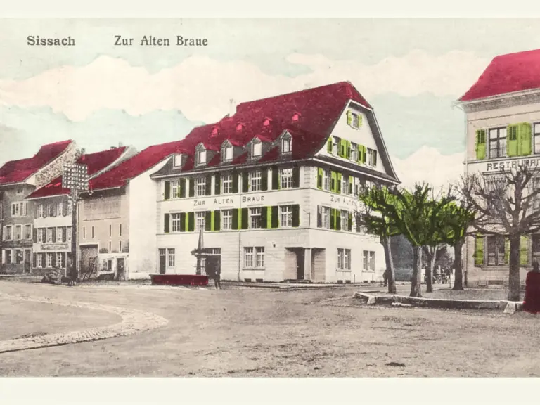 Altes Gasthaus mit rotem Satteldach und grünen Fensterläden an einem Dorfplatz.