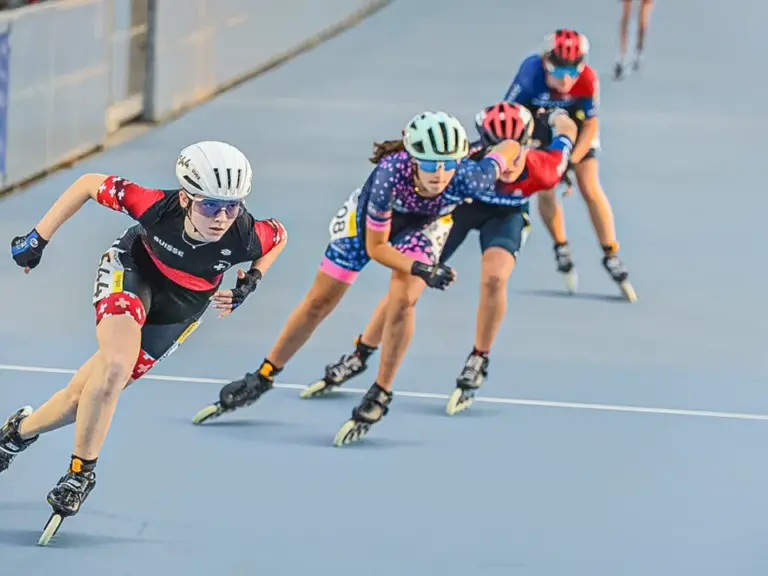 Gruppe von Inline-Speedskaterinnen in Schräglage bei voller Fahrt auf einer Rundbahn.